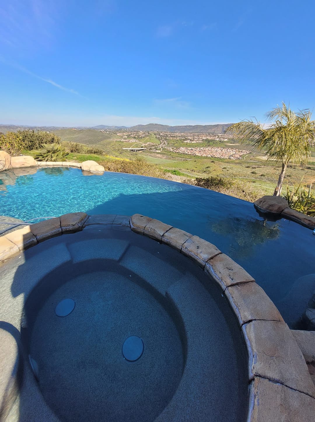 Luxury hot tub overlooking scenic valley and clear blue sky, ideal for relaxation.