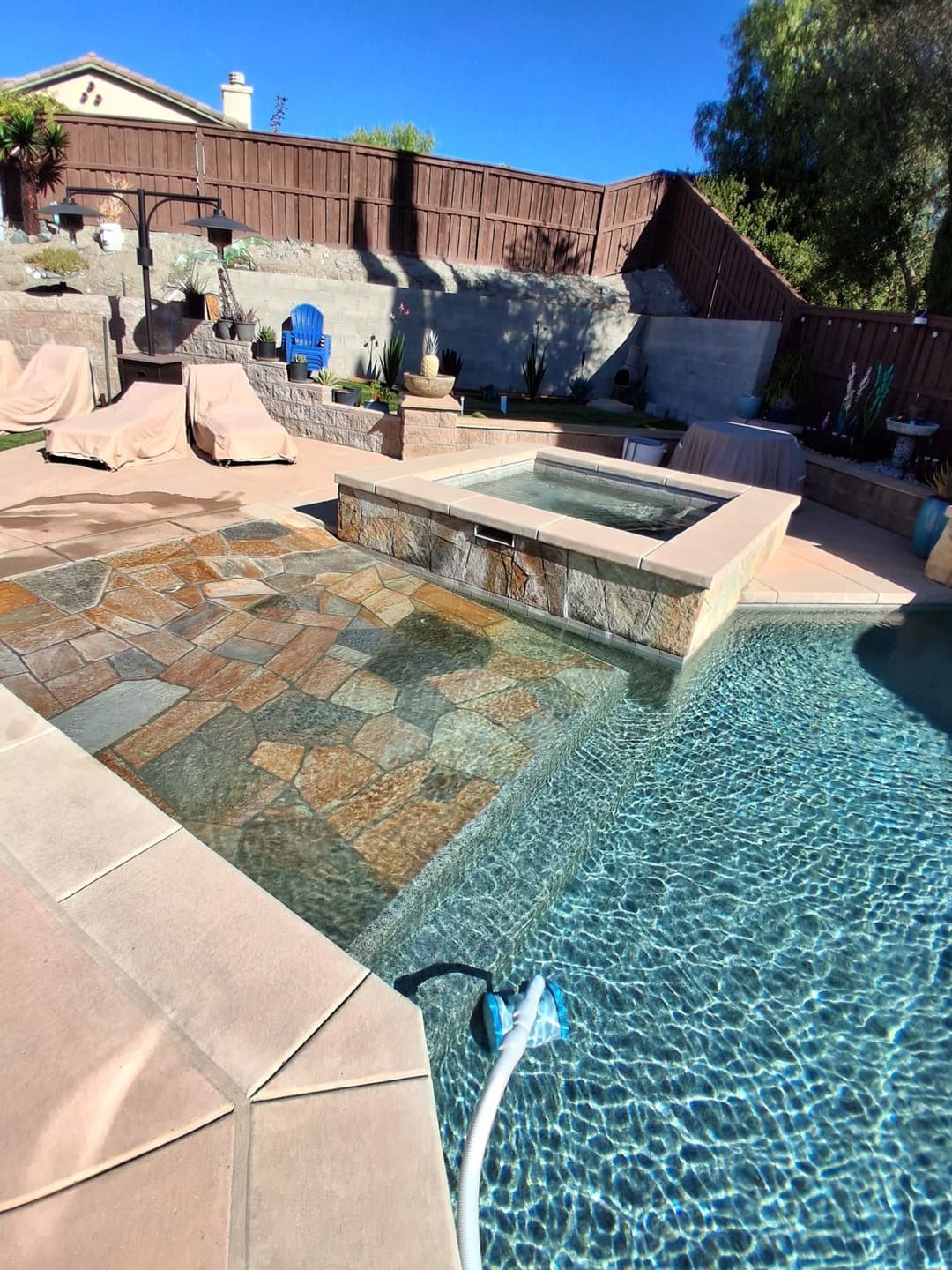 Sparkling pool with spa, stone patio, and lounge chairs in a sunny backyard oasis.