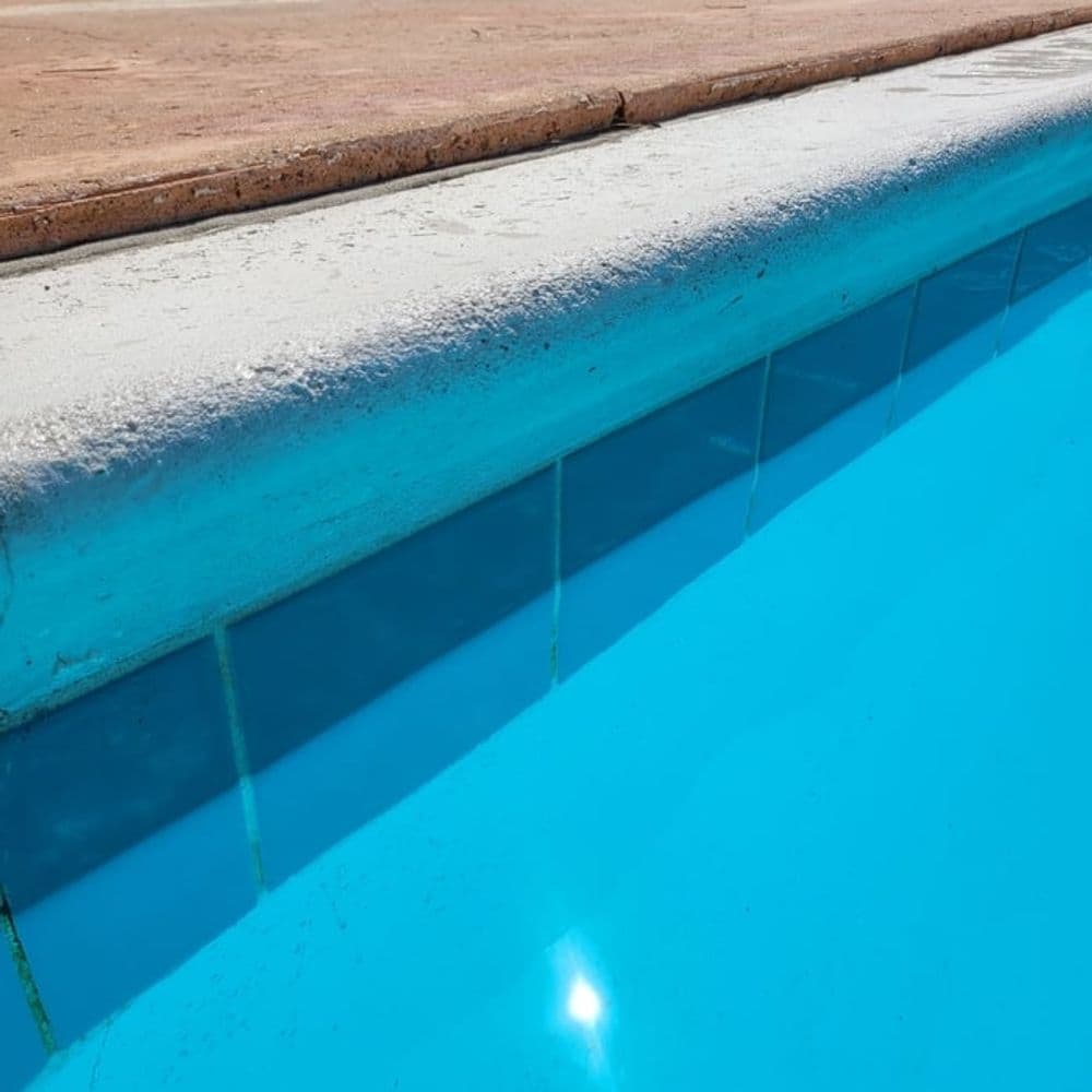 Close-up of a clear blue swimming pool edge with tiled border and sun reflections.