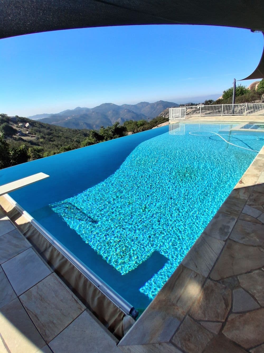 Infinity pool overlooking mountain range with clear blue sky and vibrant water reflections.