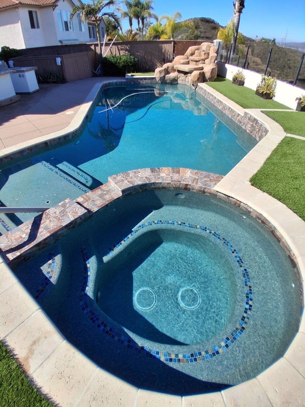 Luxury swimming pool and spa with stone features, surrounded by lush landscaping.