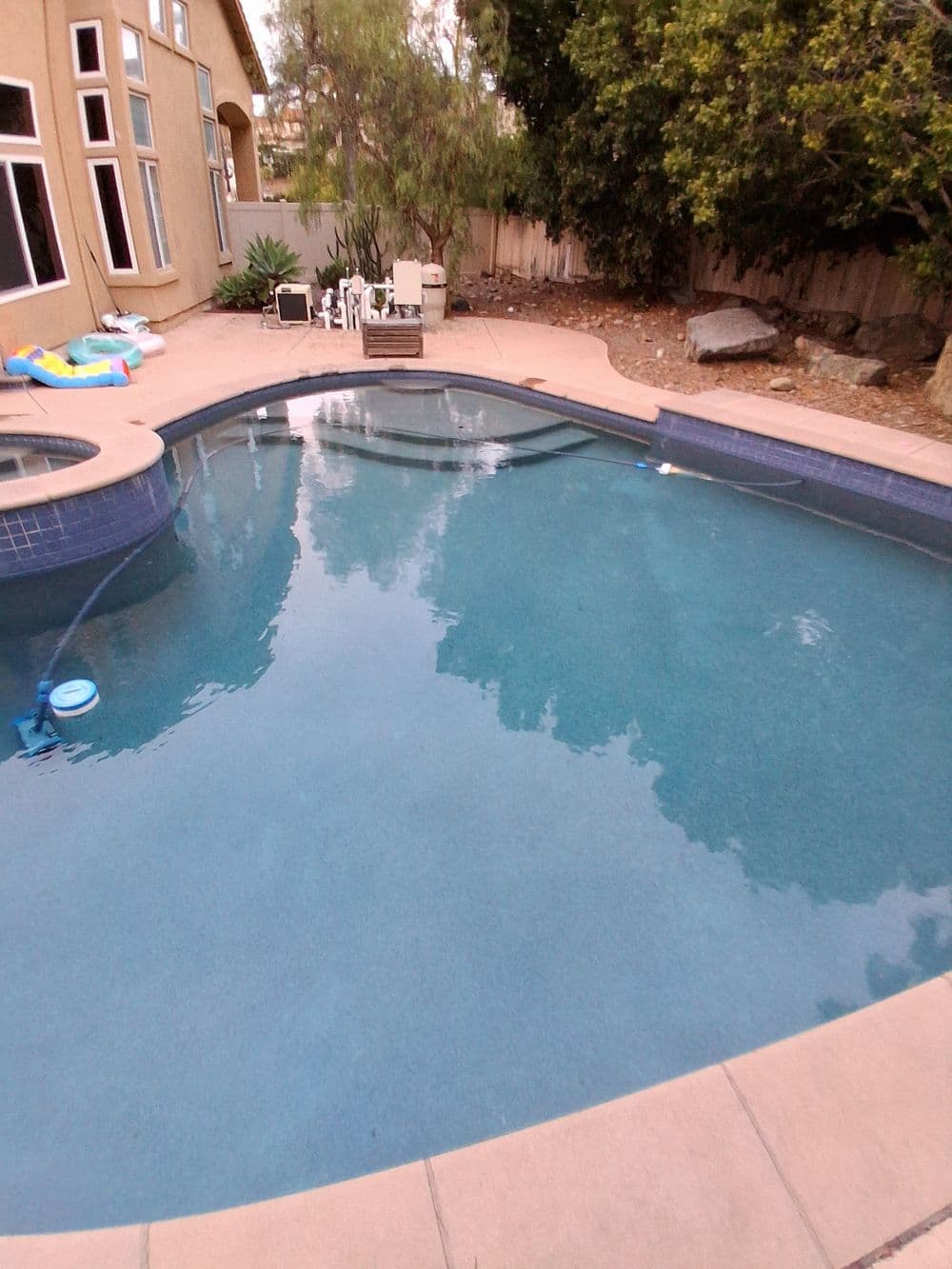 Backyard swimming pool surrounded by trees and a patio area with seating.