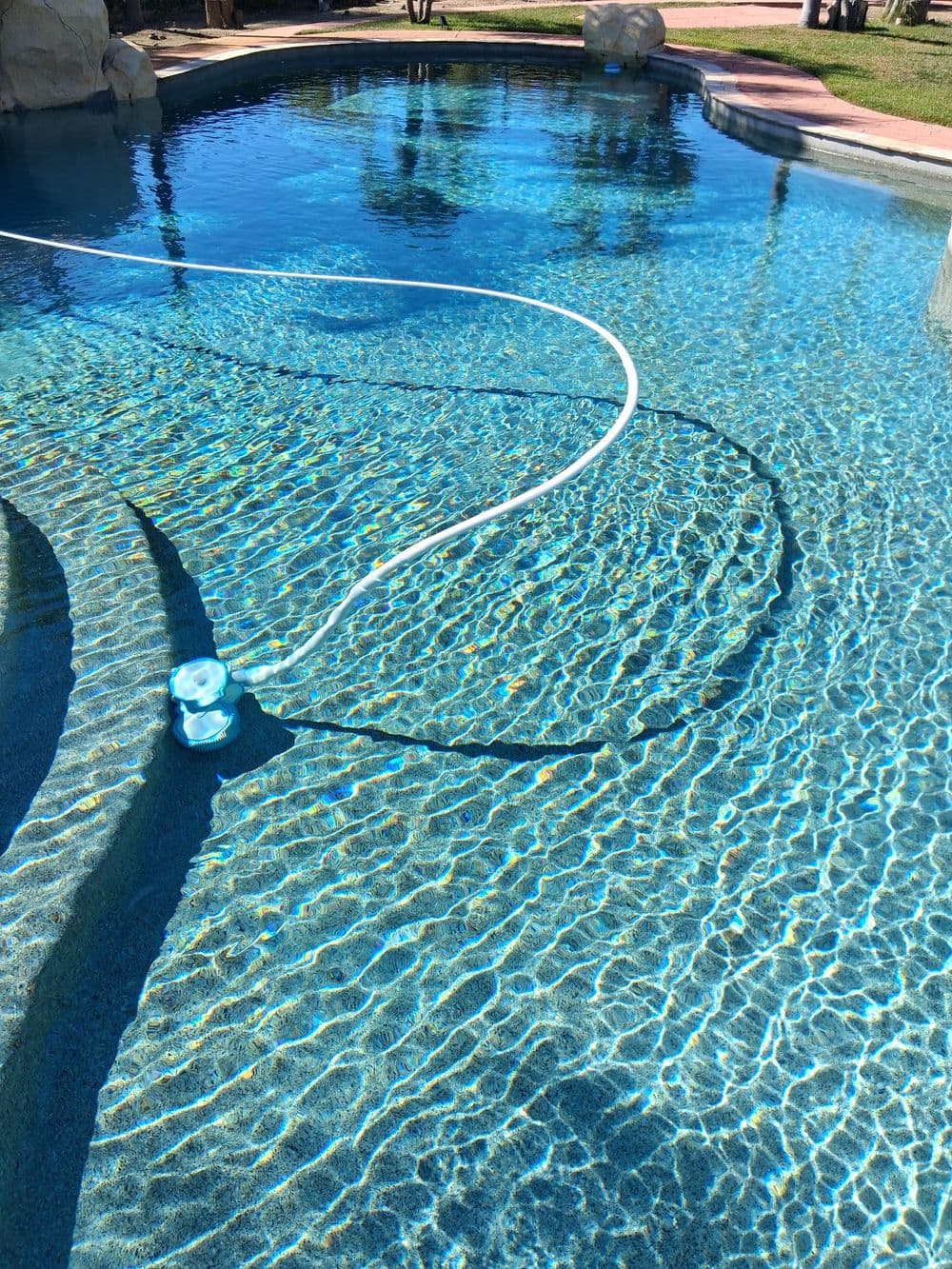 Clear blue swimming pool with a pool cleaner and sunlight reflections on the water surface.