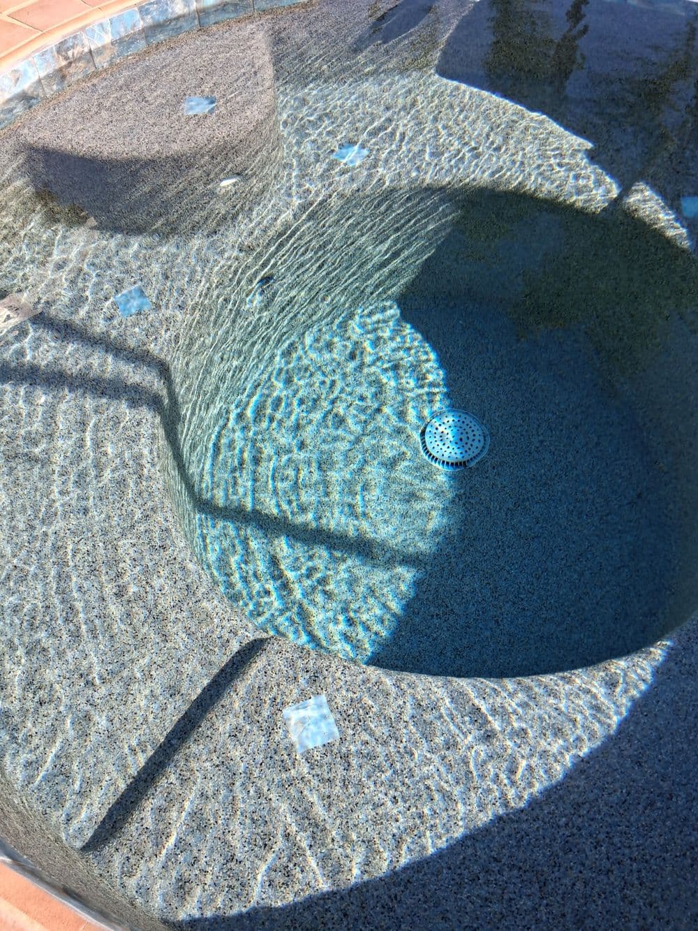 Round hot tub with textured surface and clear water reflecting sunlight outdoors.